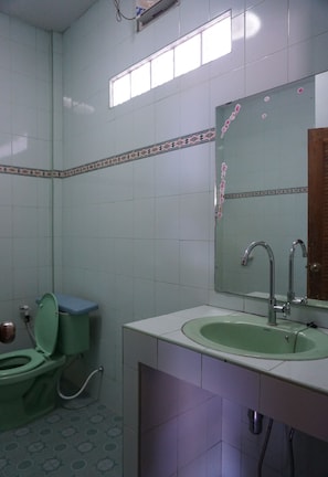 Un baño con inodoro verde, lavamanos y espejo.