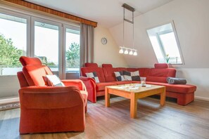 Uma sala de estar moderna com sofás vermelhos, uma mesa de centro de madeira e grandes janelas com vista para o verde lá fora.