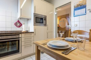 Cozinha moderna com armários brancos, forno embutido, micro-ondas e mesa de jantar posta com pratos, copos e talheres.