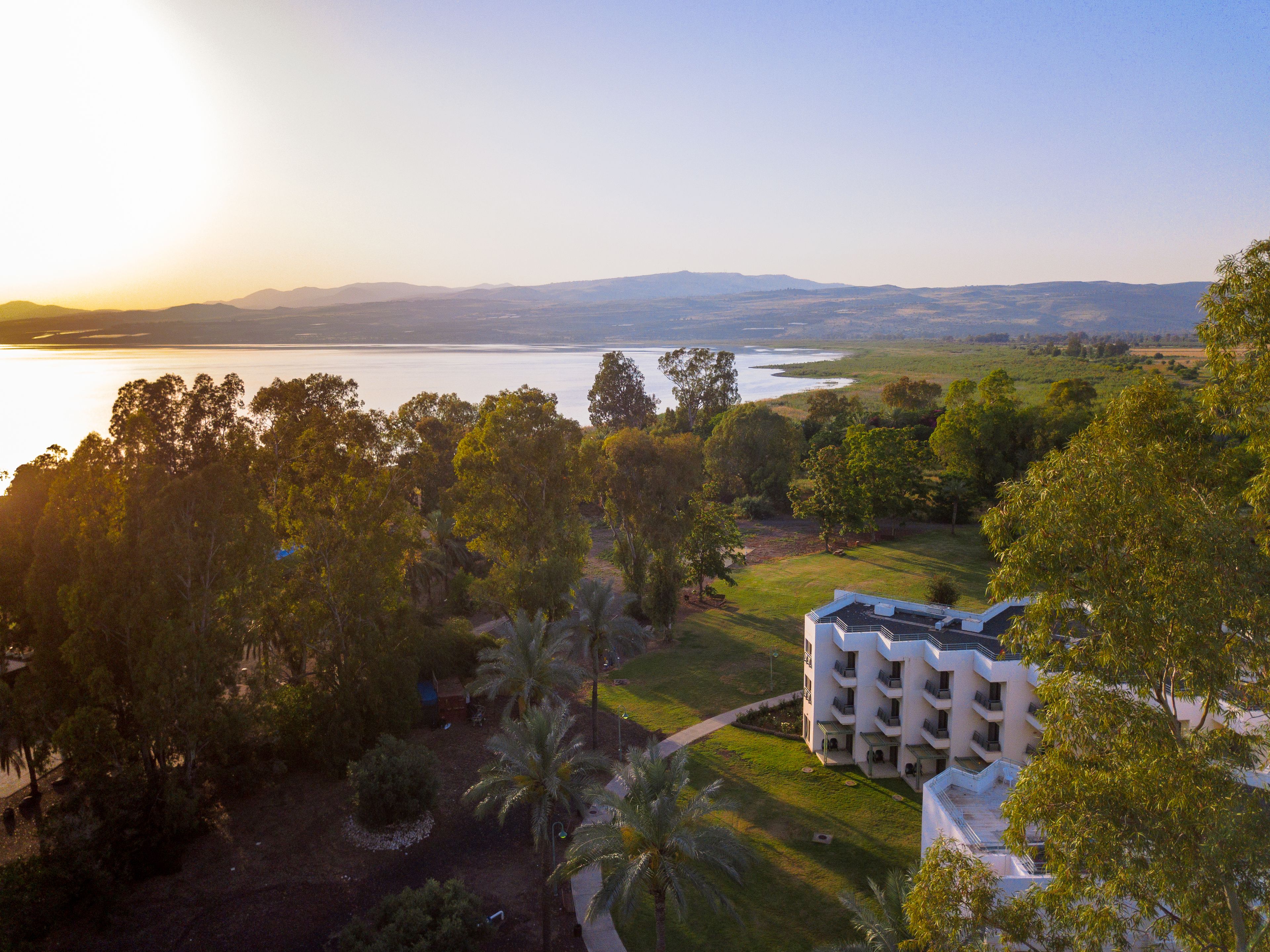 A hotel with a modern design, located near a body of water with a view of distant mountains.