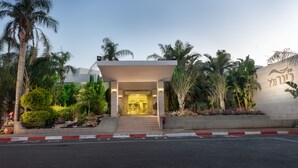 A hotel entrance with a covered walkway, palm trees, and a well-maintained garden. - Kinar Galil (Ramot)