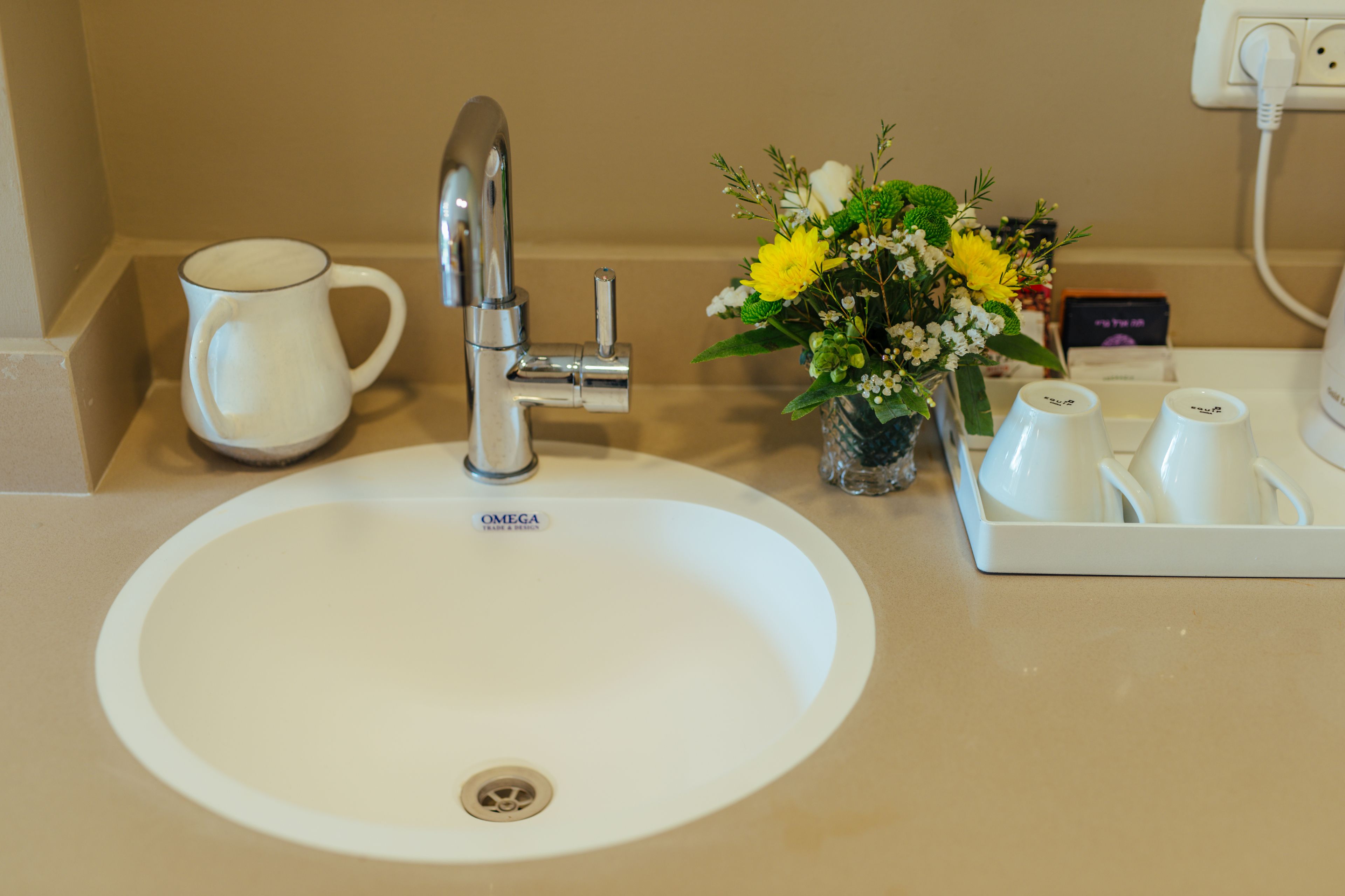 Un lavamanos con grifo, una taza blanca, un florero con flores y una bandeja con tazas.