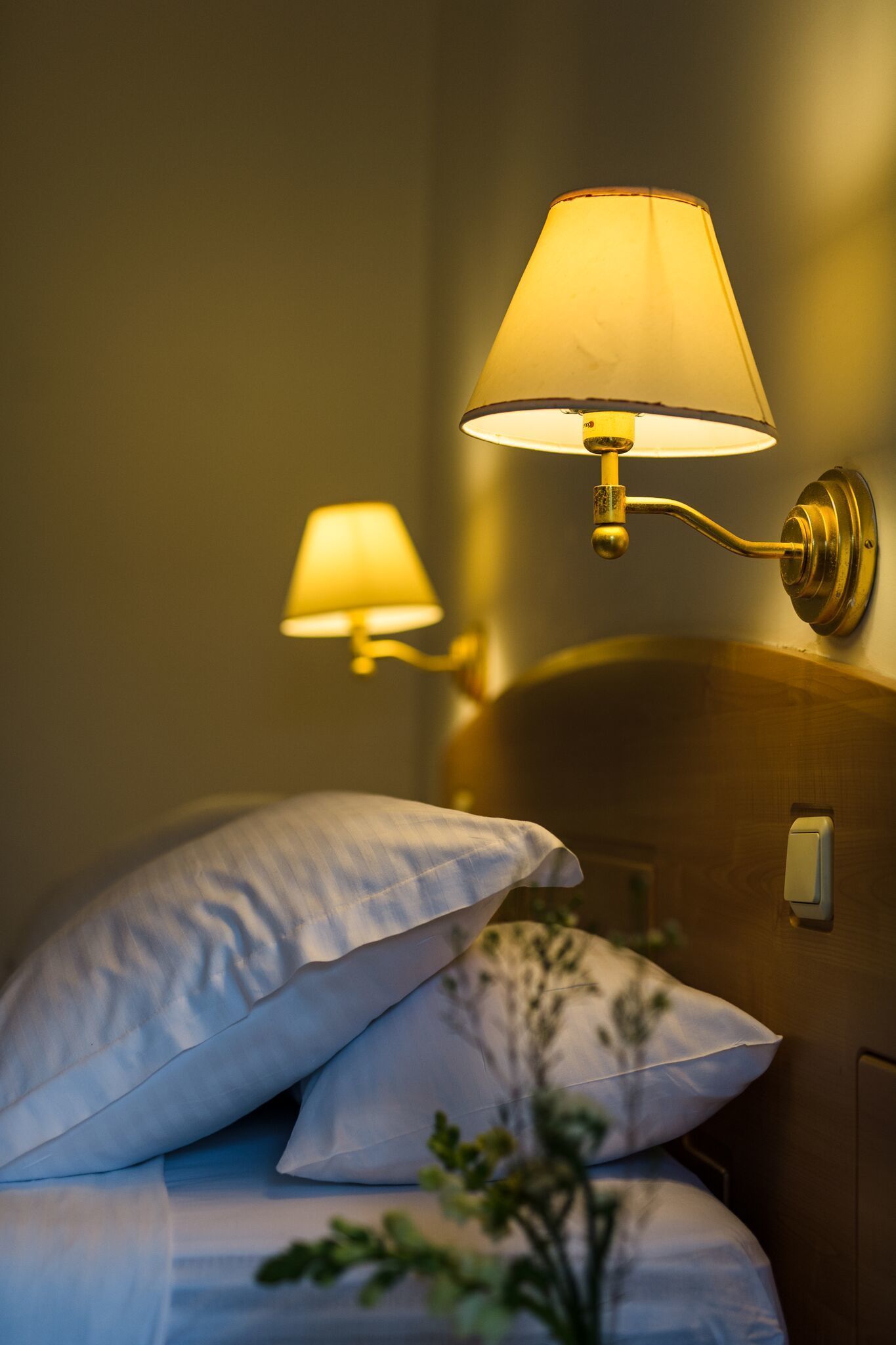 Een hotelkamer met een bed, kussens en een lampje aan de muur.