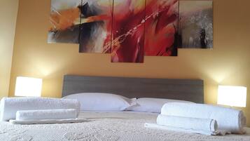 A hotel room with a bed, white towels, and a large abstract painting on the wall.
