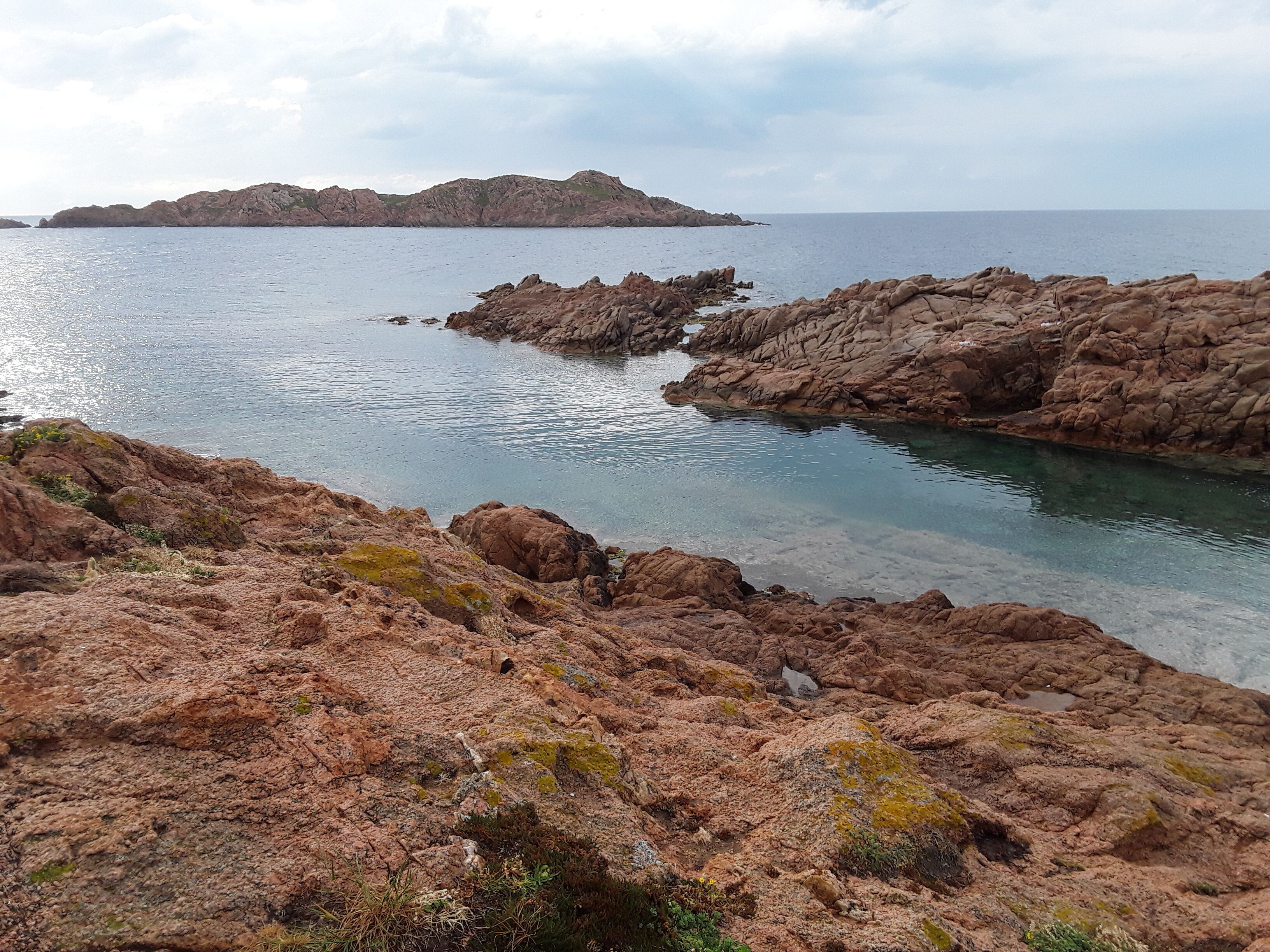 Un paisaje costero rocoso con aguas cristalinas y colinas a lo lejos.