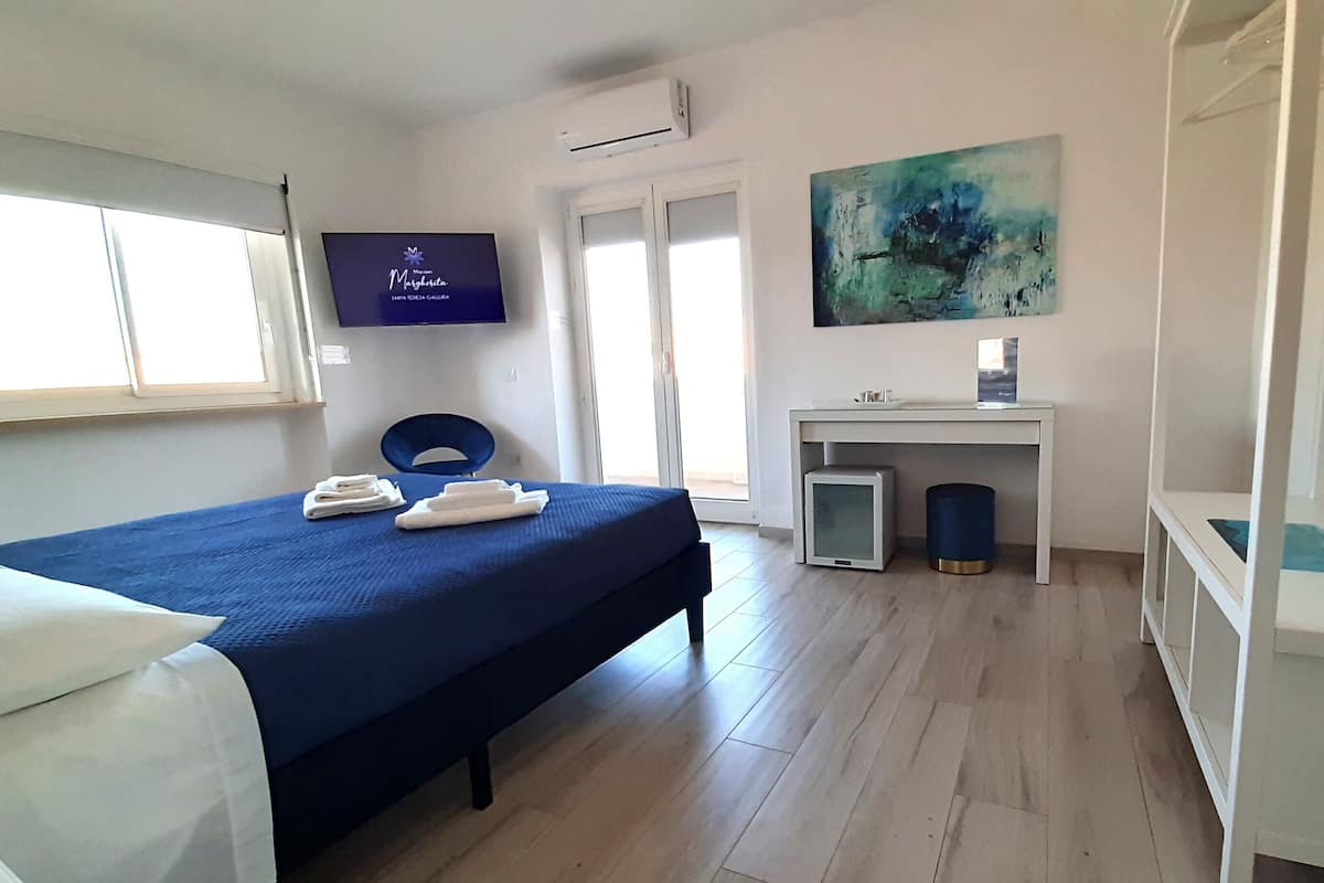 A hotel room with a bed, a desk, a TV, and a painting.