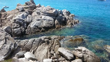 Una costa rocosa con agua azul cristalina, barcos y un yate a lo lejos.
