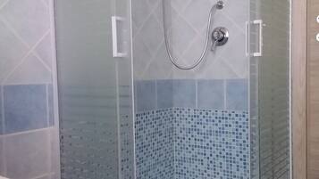 Eine separate Duschkabine mit gefliestem Boden und Wänden, einer Handbrause und einem am Wand montierten Wasserhahn.