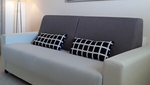 Una sala moderna con un sofá, dos almohadones estampados, una lámpara de pie y un cuadro grande en la pared.
