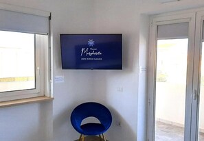 A room with a mounted television displaying 'Marion Margherita Santa Teresa Gallura,' a blue chair, and a sliding glass door.