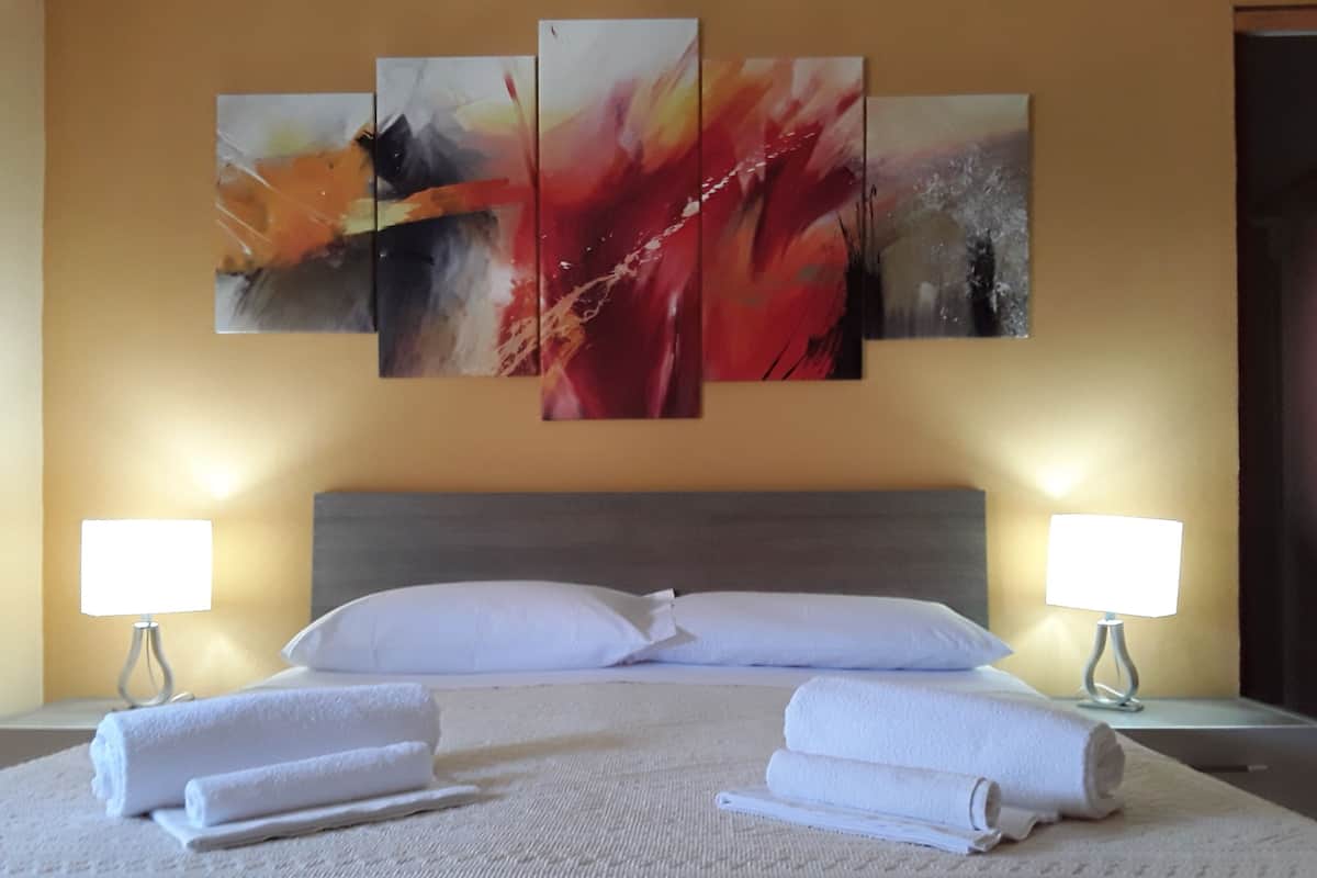 A hotel room with a large bed, two bedside lamps, and three abstract paintings on the wall.