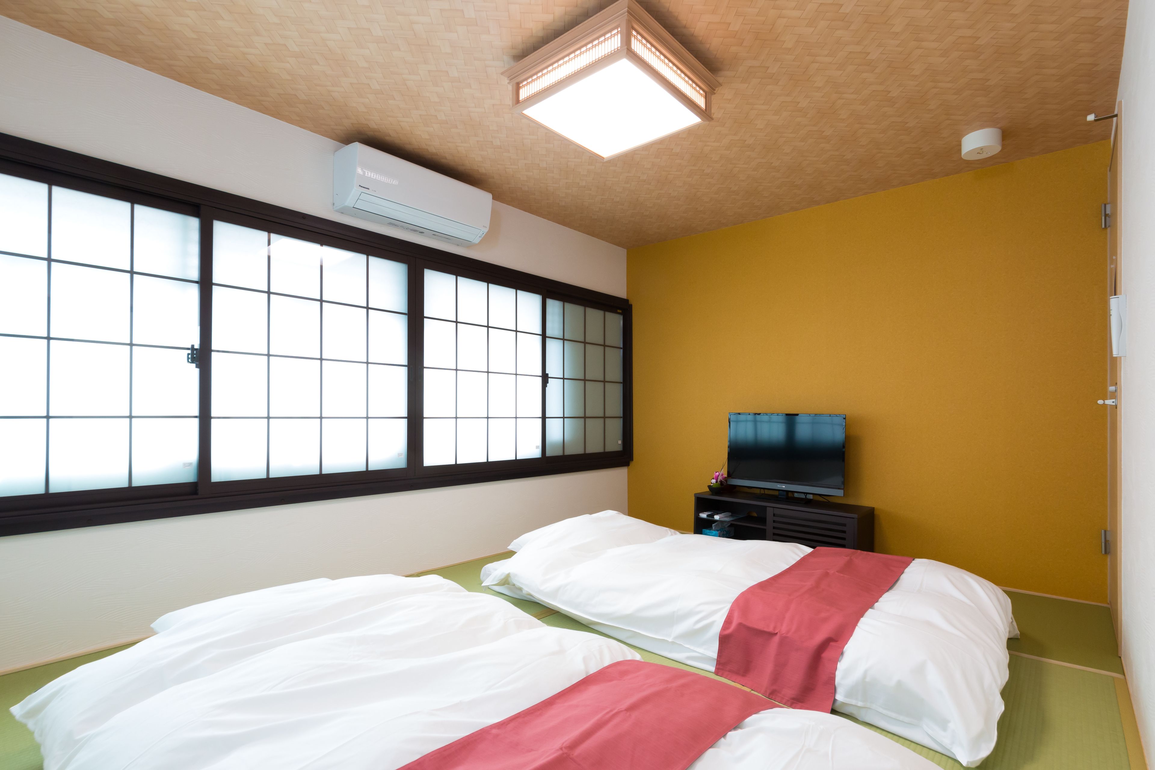 Ein Hotelzimmer mit großem Fenster, einem Bett mit weißer und roter Bettwäsche, einem Flachbildfernseher und einer Klimaanlage.