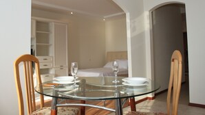 Un comedor con mesa de vidrio, sillas de madera y un armario blanco al fondo.