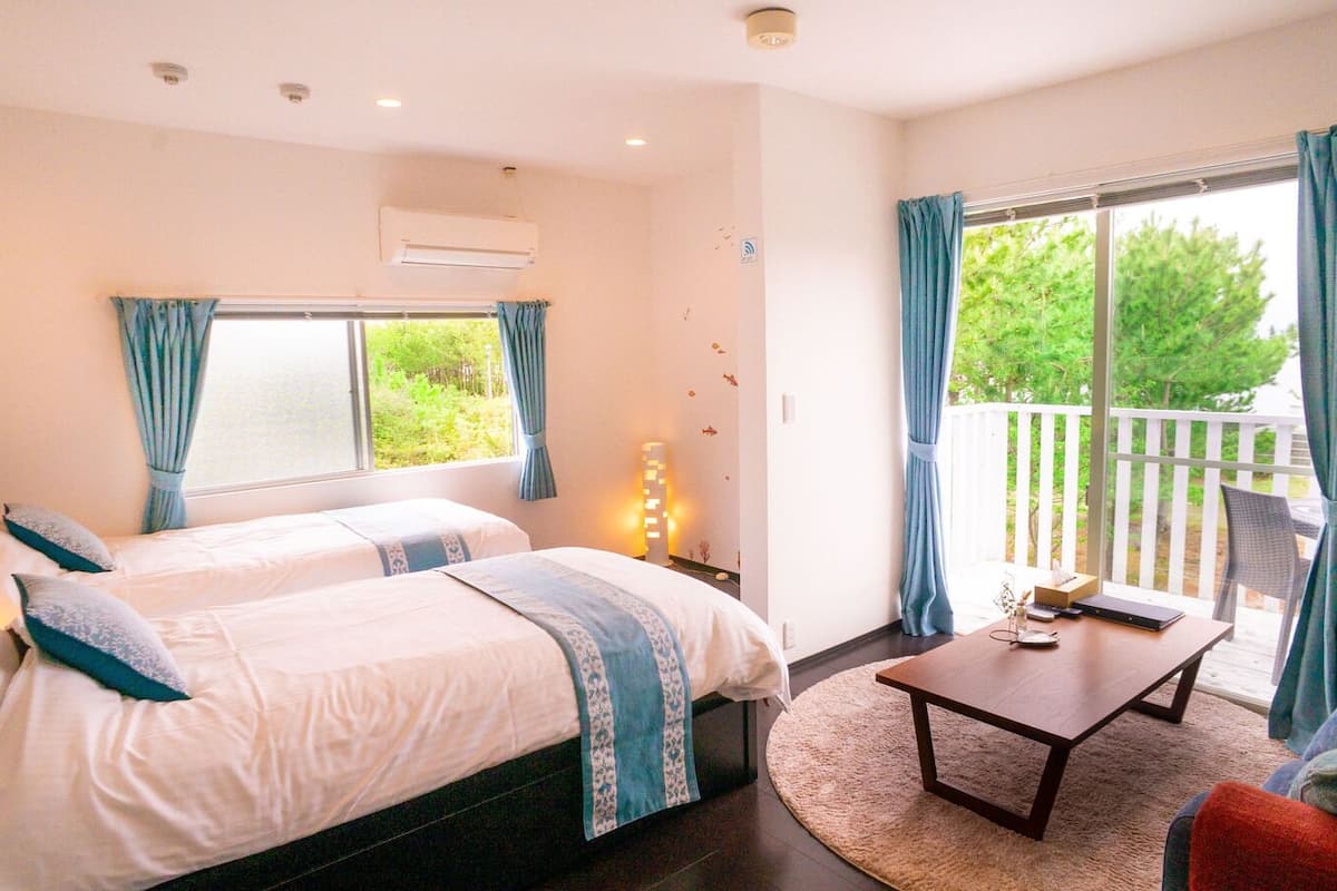 A hotel room with two beds, a sofa, a small table, and a balcony with curtains.