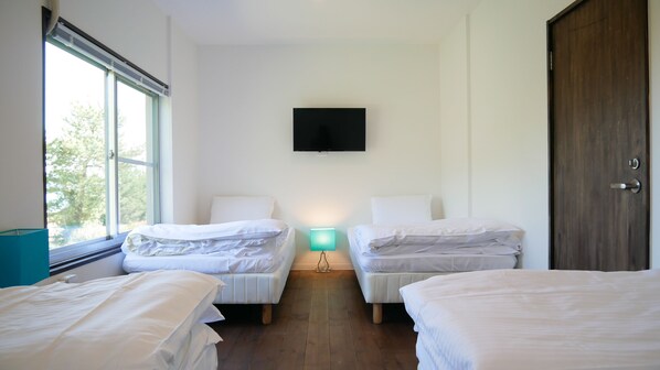 Une chambre d’hôtel avec deux lits simples, un téléviseur fixé au mur et une fenêtre donnant sur la verdure.