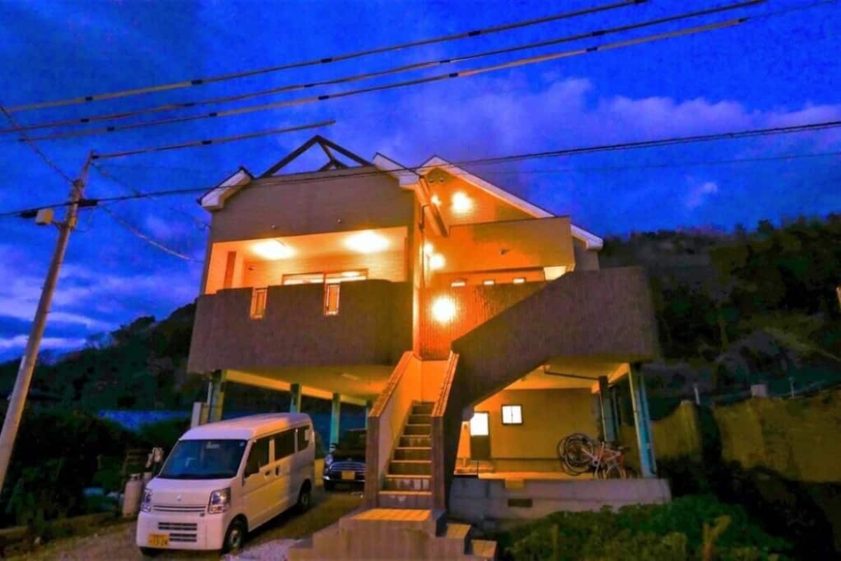 A two-story building with a staircase leading to the upper level, a parked van, and a bicycle.