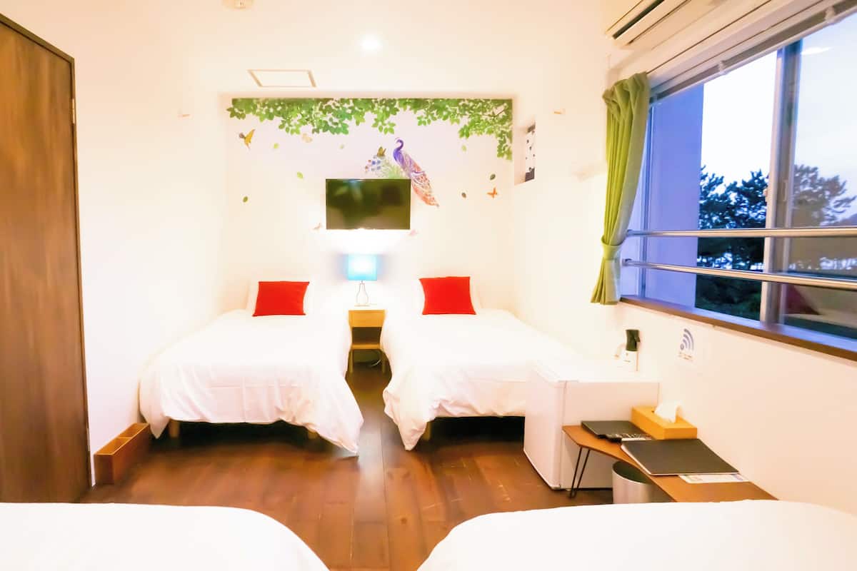 A hotel room with two beds, a TV, a desk, and a window with curtains.