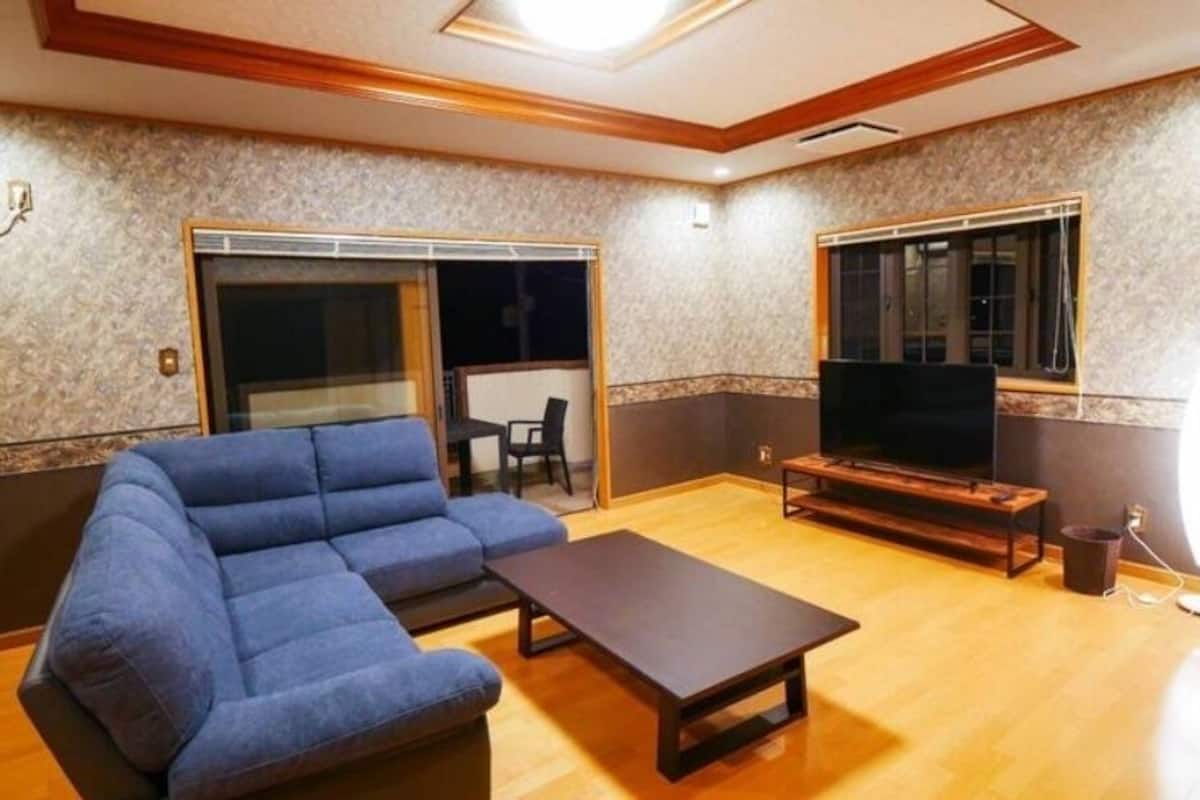 A living room with a blue sofa, a coffee table, a TV stand, and a sliding glass door.