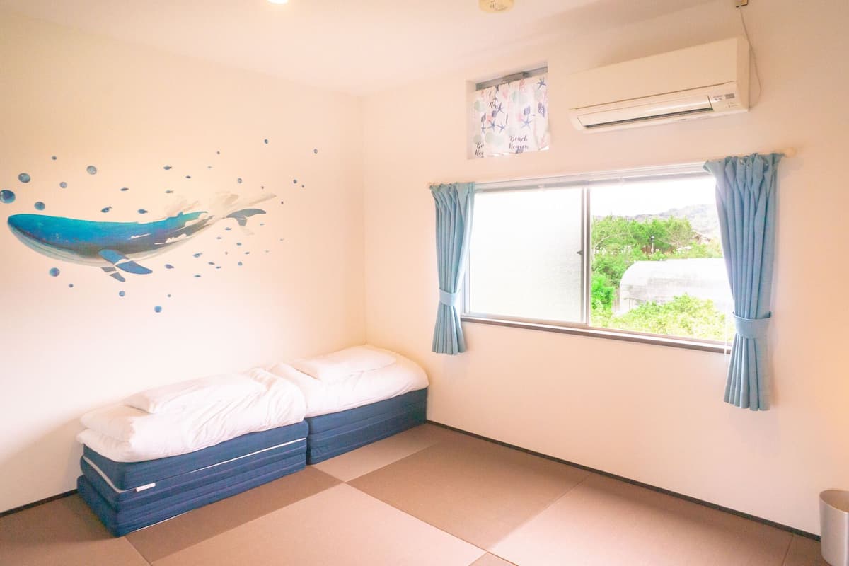 A bedroom with a bed, a window with curtains, an air conditioner, and a wall decoration of a whale.