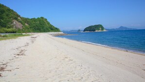 A beach with a sandy shore, a small island in the distance, and a clear blue sky.