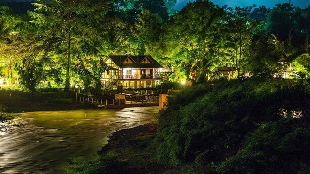 A two-story lodge with a balcony overlooking a river, surrounded by dense forest. - Muang La Lodge (Muang La)
