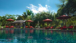 A swimming pool with red lounge chairs and umbrellas, surrounded by lush greenery and a traditional building. - Muang La Lodge (Muang La)