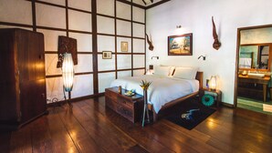 A bedroom with a wooden floor, a bed with white linens, a dresser, a nightstand with a lamp, and a painting on the wall. - Muang La Lodge (Muang La)