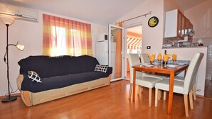 A cozy living area with a sofa, a dining table set for four, and a kitchenette in the background. - Apartments Jeromela (Fazana)