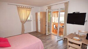 A bedroom with a bed, a desk with a chair, a TV, and a sliding glass door leading to an outdoor area. - Apartments Jeromela (Fazana)