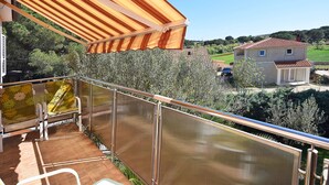 A balcony with a metal railing, a covered area with striped fabric, and a view of a house with a red-tiled roof. - Apartments Jeromela (Fazana)