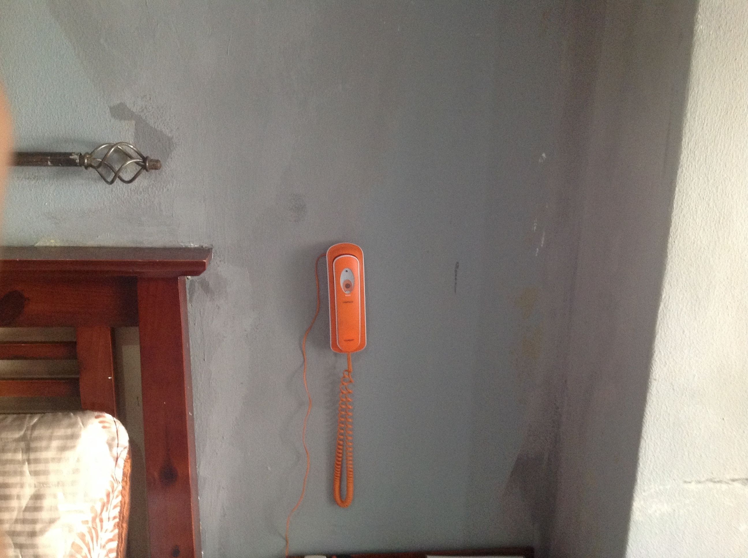 A room with a wooden bed frame, a wall-mounted telephone, and a visible door handle.