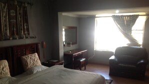 Un dormitorio con cama, escritorio, silla y un amplio ventanal con cortinas.