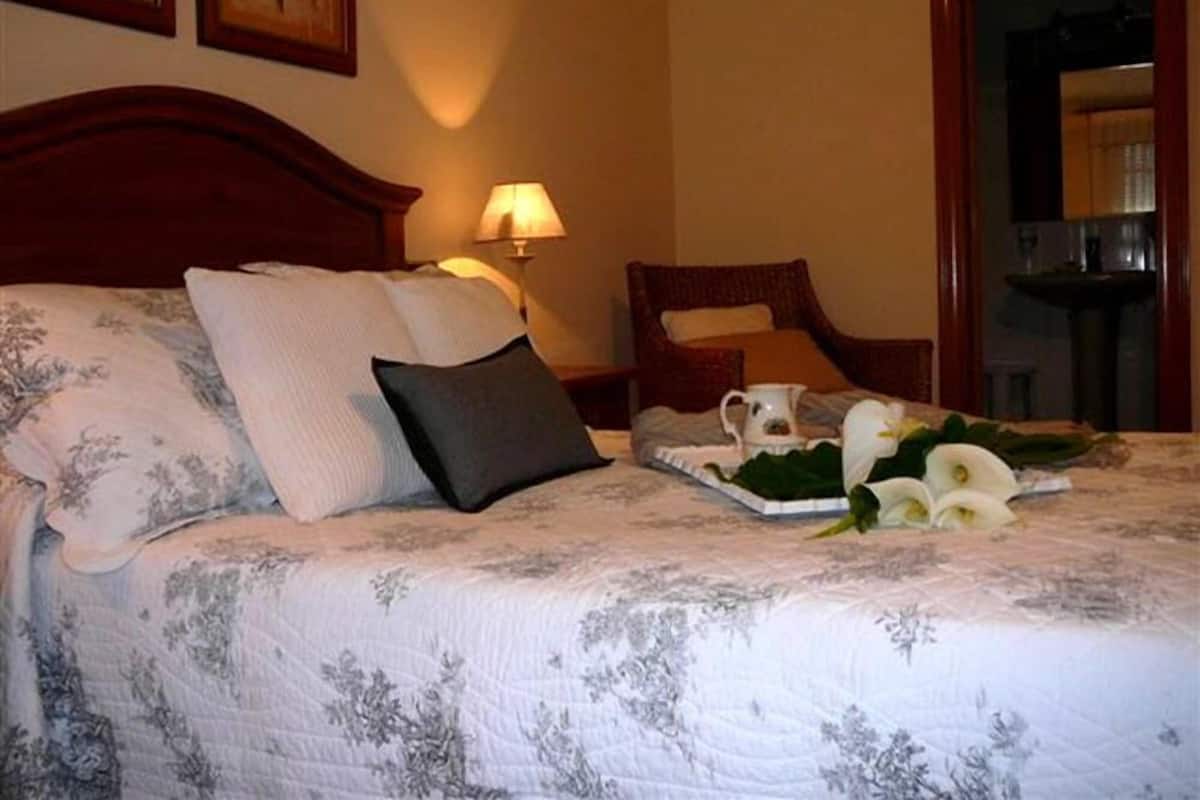 A neatly made bed with floral bedding, a bedside table with a lamp, and a tray with flowers and a pitcher.