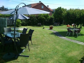 A patio with a table and chairs, a large umbrella, and a brick house in the background. - Casa de Grande (Cambados)