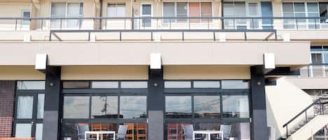 A modern building with a two-story structure, large windows, and outdoor seating area with tables and chairs.