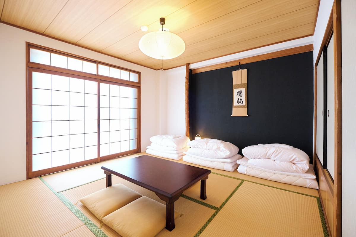 Una habitación japonesa tradicional con suelo de tatami, una mesa de madera baja y ropa de cama blanca.