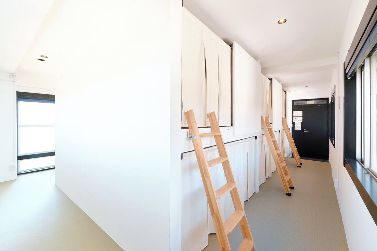 Un pasillo con paredes blancas, una escalera de madera apoyada en una pared, y una puerta al final.