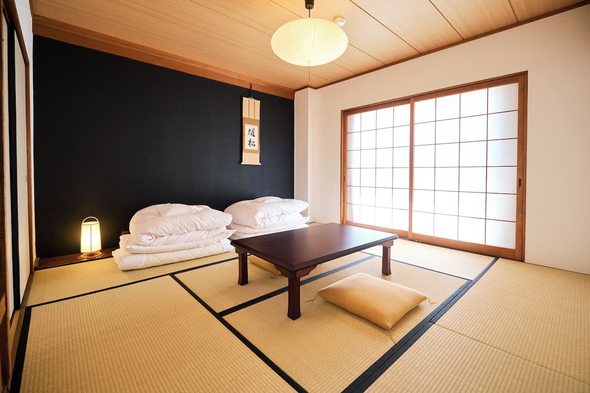 Una habitación japonesa tradicional con suelo de tatami, una mesa de madera baja y ropa de cama blanca.