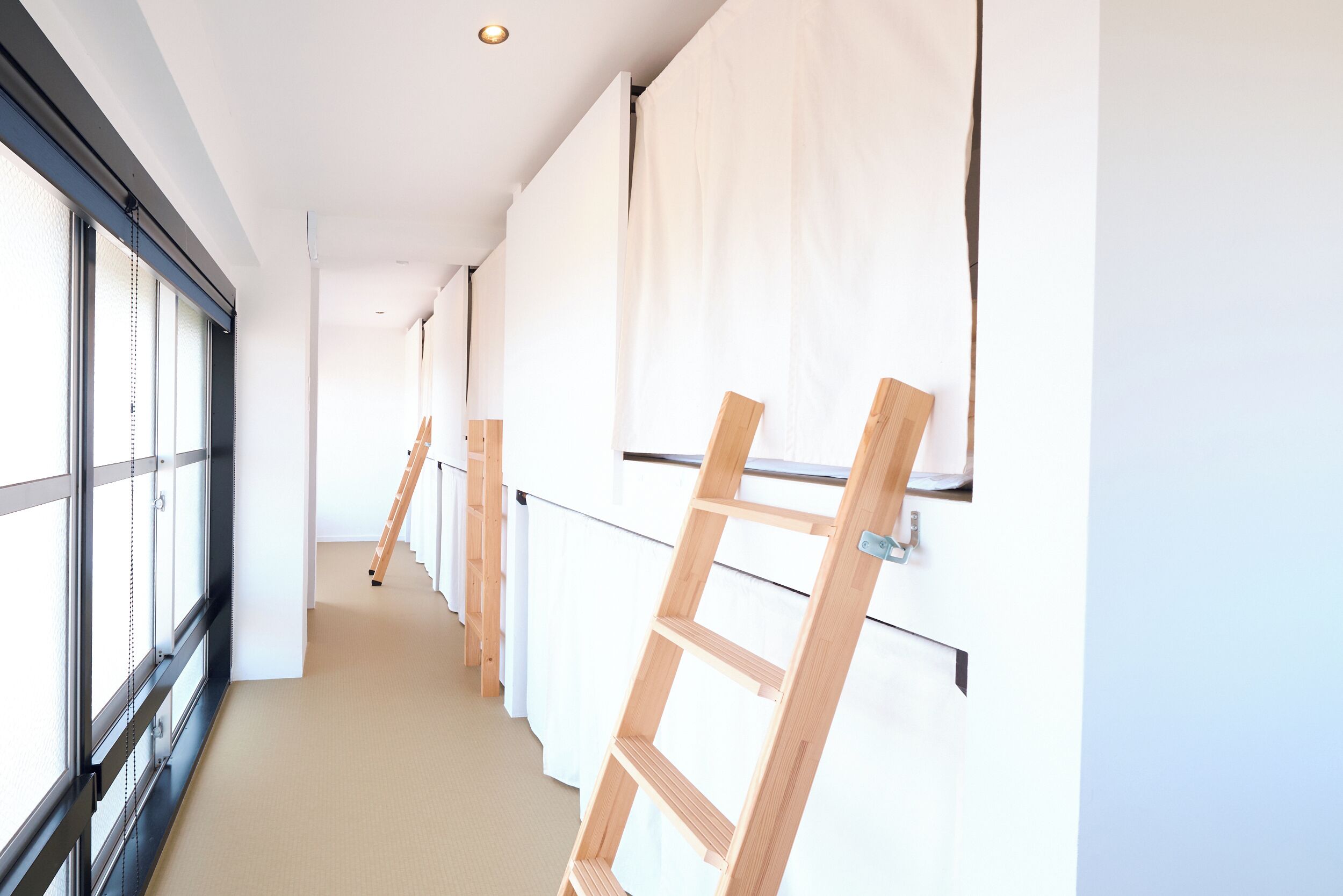 Un pasillo con escaleras de madera apoyadas en las paredes, ventanas amplias y una alfombra color beige.