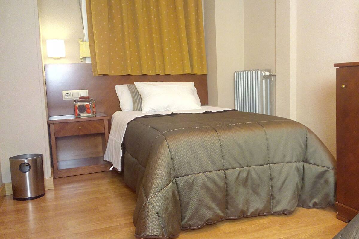 A hotel room with a bed, a nightstand, a lamp, a radiator, and a TV.