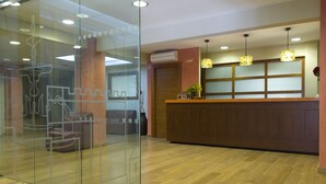 A reception area with a wooden reception desk, glass partition, and a ceiling with recessed lighting. - Hotel Avenida (Requena)
