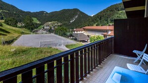 Un balcon donnant sur un paysage montagneux, un espace de stationnement et un bâtiment avec un toit rouge.