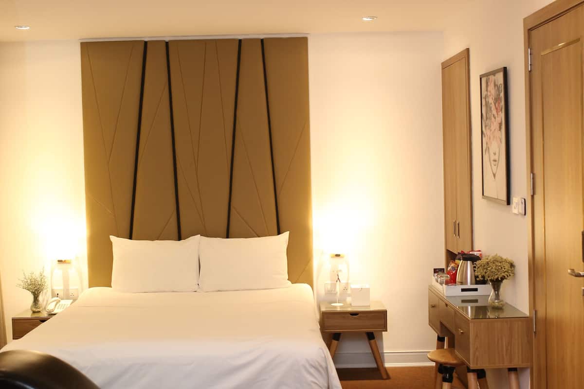 A modern hotel room with a large bed, bedside tables, a desk, and a wardrobe.