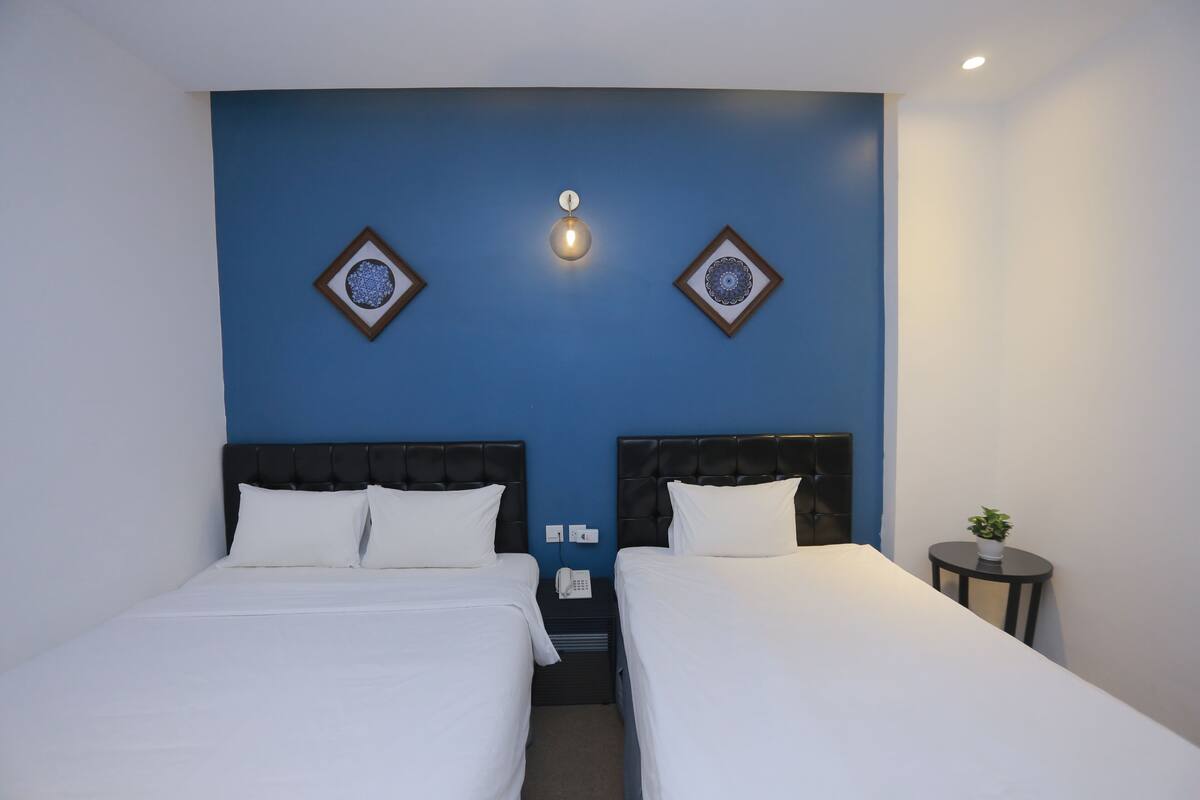 A hotel room with two beds, a small table with a plant, and a wall-mounted light fixture.