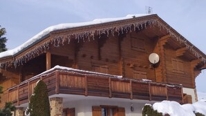 Un chalet en bois doté d’un balcon, avec des fondations en pierre et un environnement enneigé.