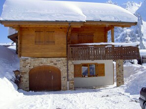 Un chalet en bois, avec des fondations en pierre, des portes en bois et un balcon doté d’une balustrade en bois.