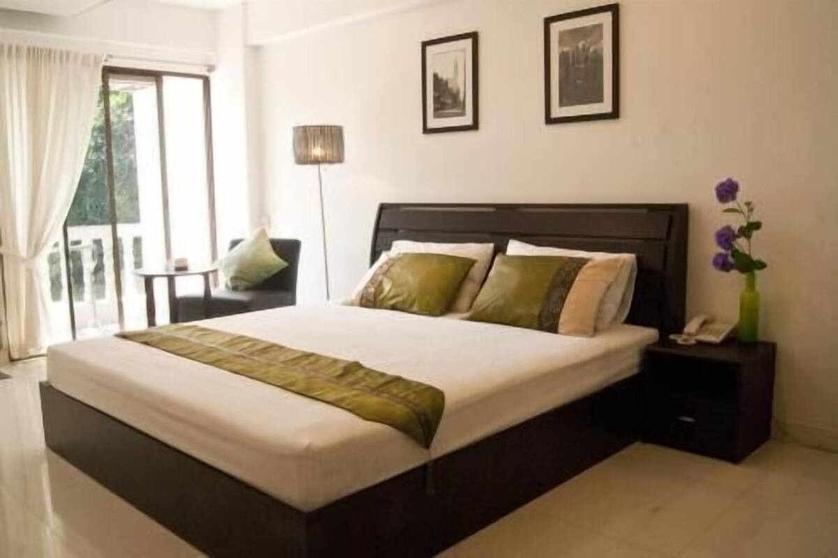 A hotel room with a large bed, a nightstand, a lamp, and a window with curtains.
