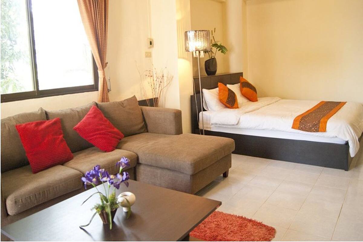 A hotel room with a sofa, a bed, a nightstand, and a lamp.