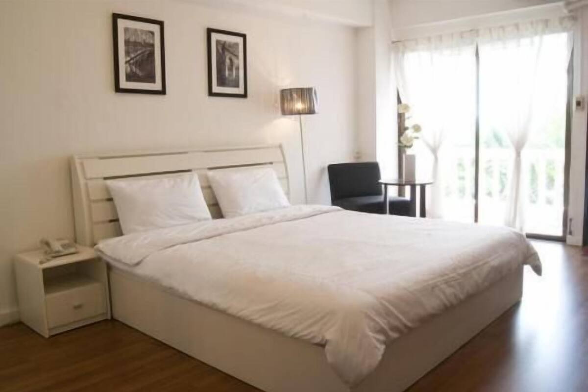 A bedroom with a bed, nightstand, lamp, chair, and two framed pictures on the wall.