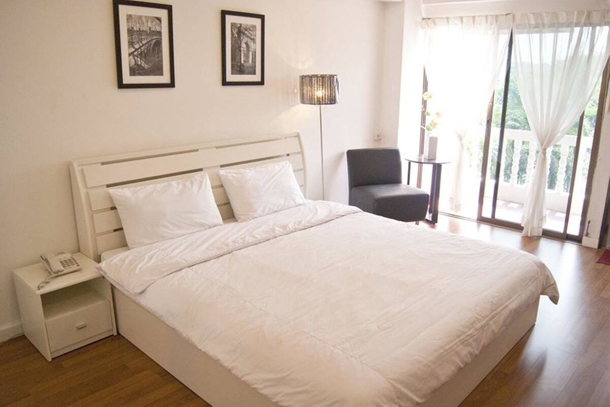A bedroom with a large bed, a bedside table with a phone, a chair, and a floor lamp.